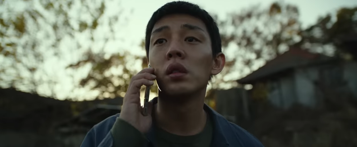 A person outdoors is holding a phone to their ear, looking thoughtful or concerned, with trees and a building in the background