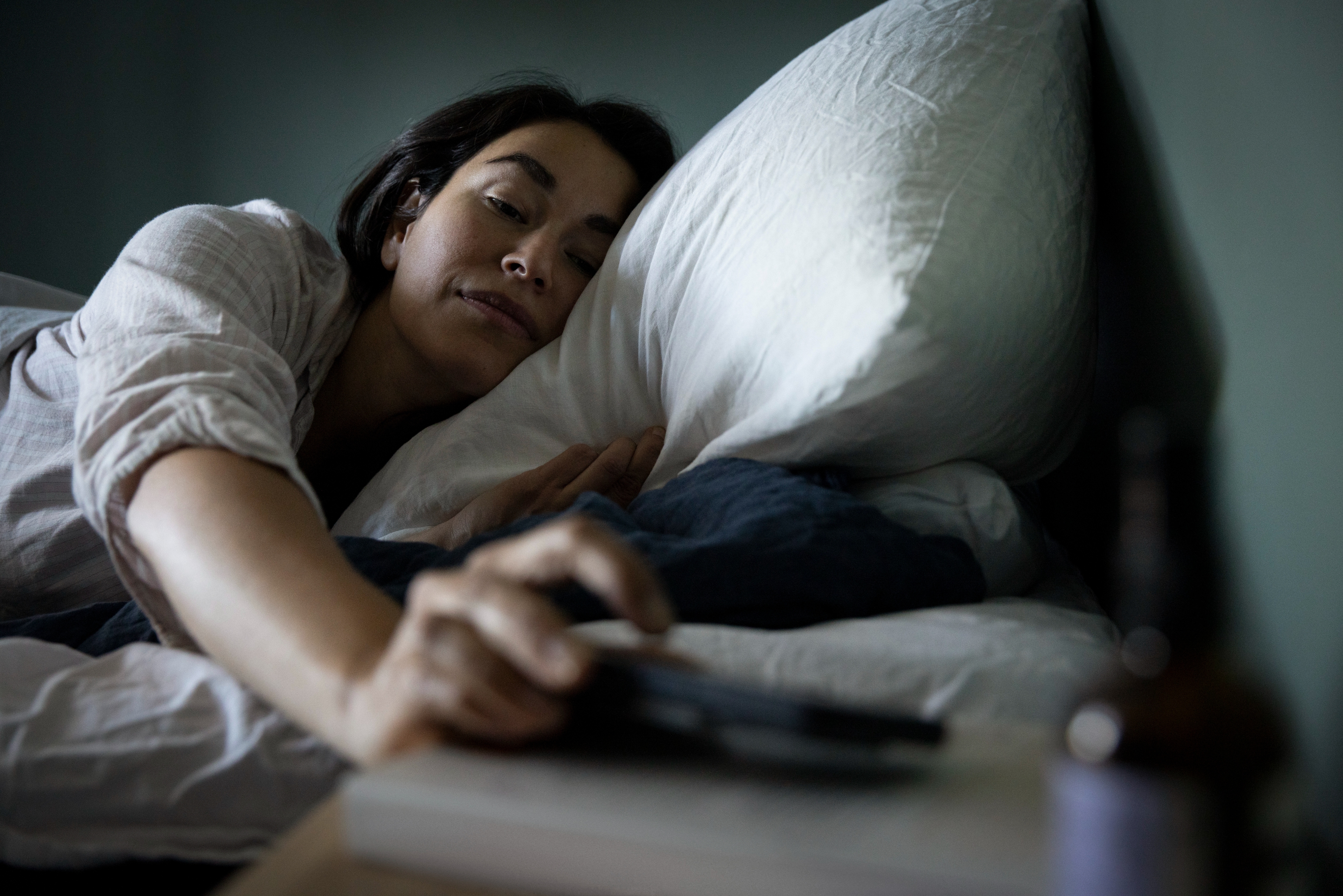 Person waking up in bed, reaching for items on a bedside table, appearing relaxed and comfortable