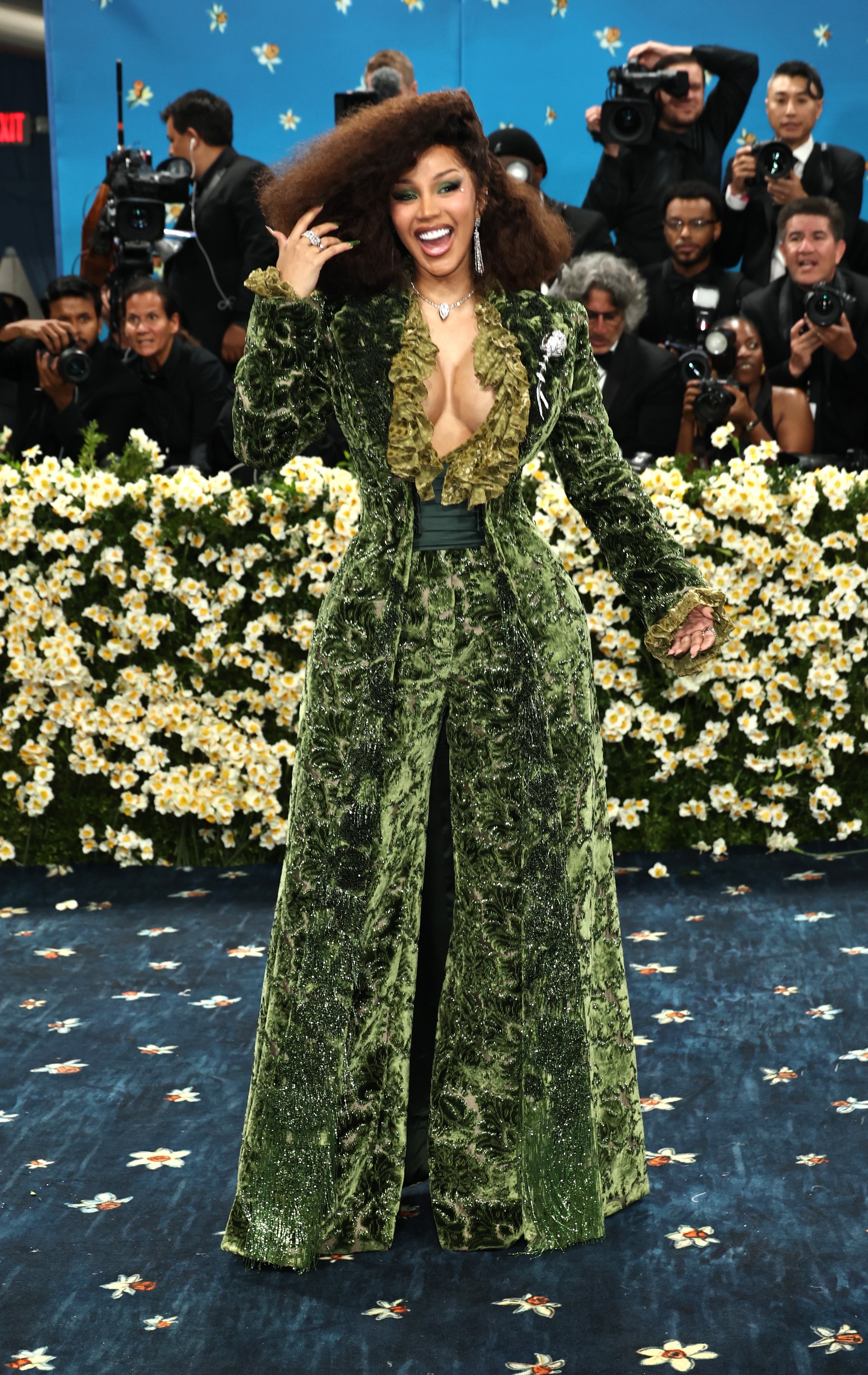 Celebrity in a luxurious, long velvet coat with a deep neckline, poses on the red carpet while photographers capture the moment