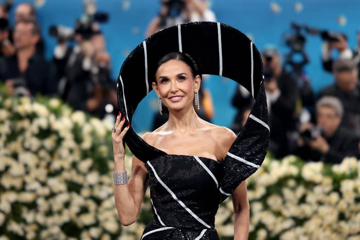 Celebrity poses on red carpet in an avant-garde, sculptural black gown with white accents, surrounded by photographers