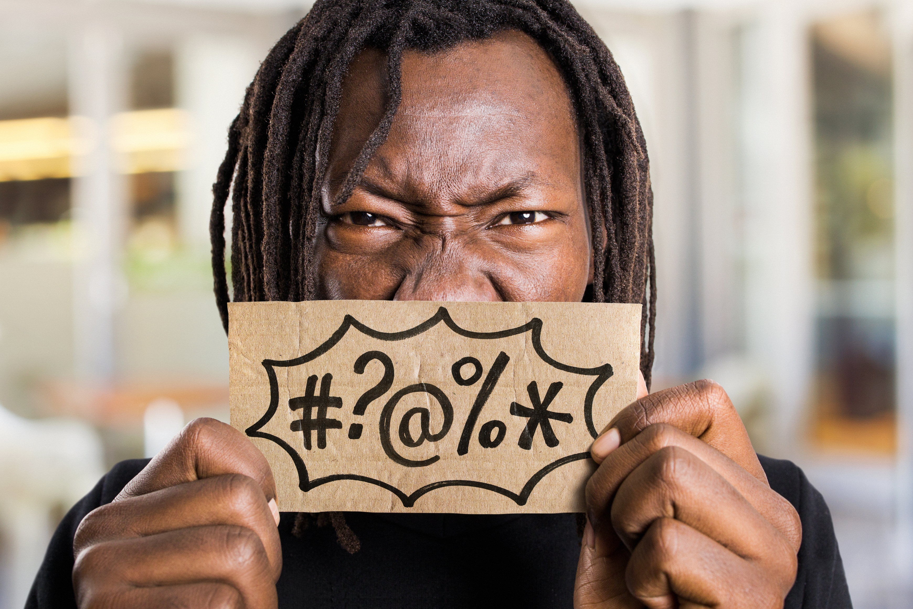 Person with an expressive face holds a cardboard sign showing symbols like #, ?, @, %, and *