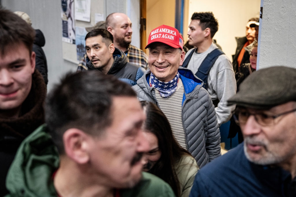 A group of people in casual attire at an indoor event; one person wears a red hat with a slogan