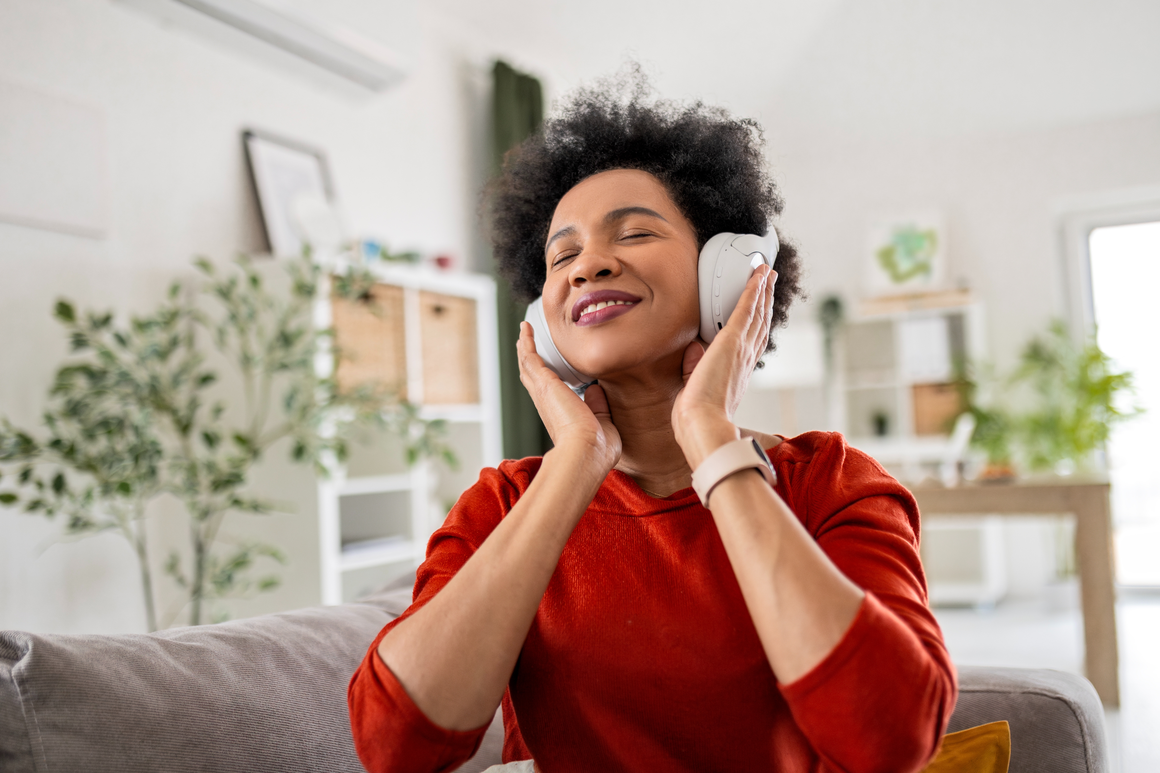 Person sitting on a couch, smiling with eyes closed, enjoying music through headphones in a cozy room