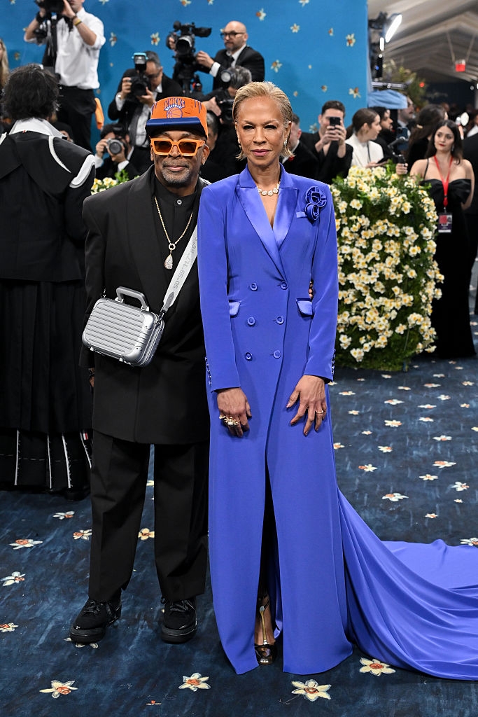 Tonya wears a bright double-breasted gown with a long skirt, Spike in a suit with a cap and sunglasses