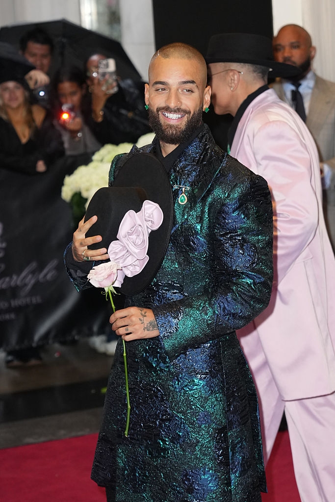 No sé quién es. Persona con abrigo brillante floral en alfombra roja, sostiene sombrero con rosa. Estilo elegante y moderno