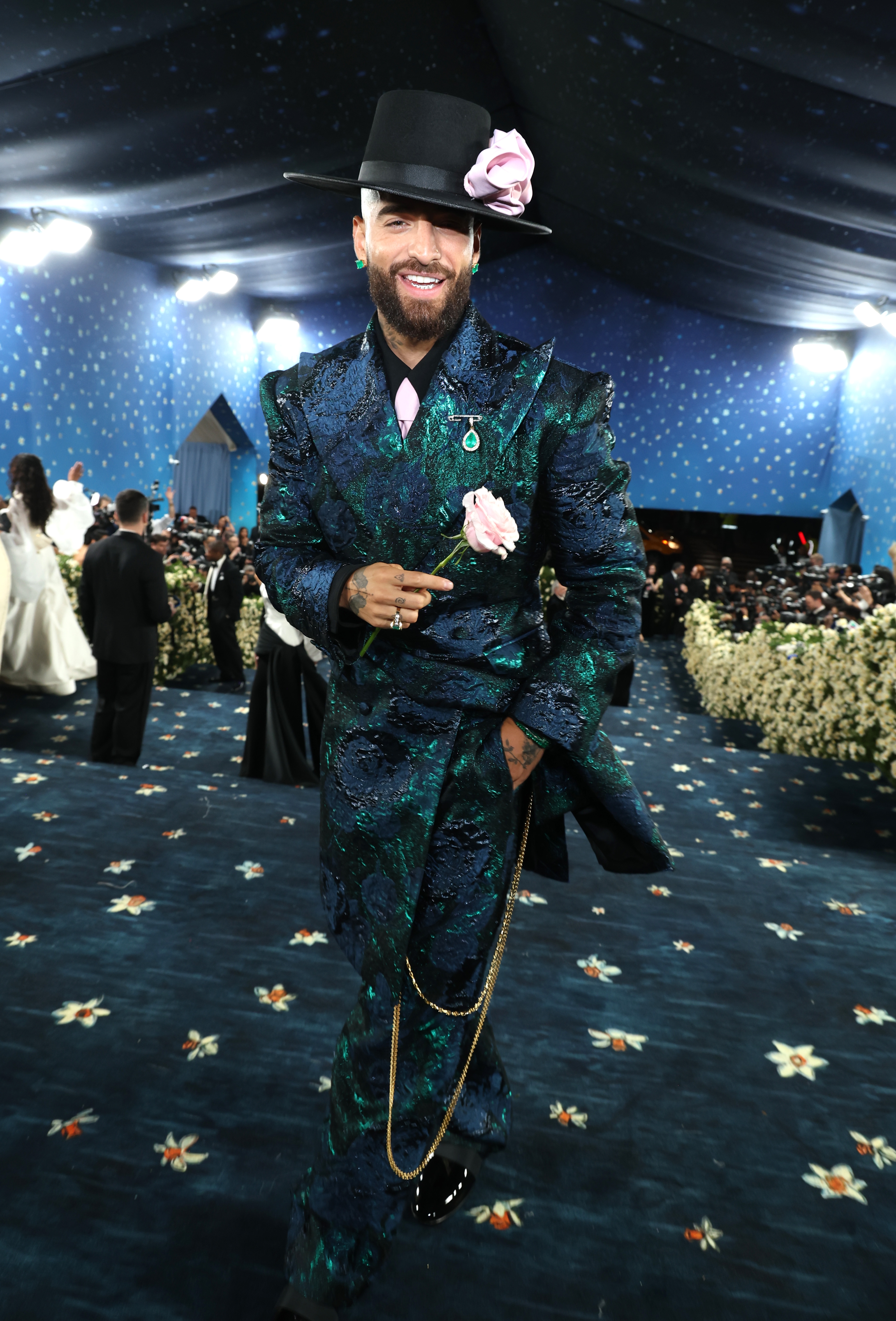 Person in a stylish patterned suit with pink flower accents and a top hat, posing confidently at a formal event