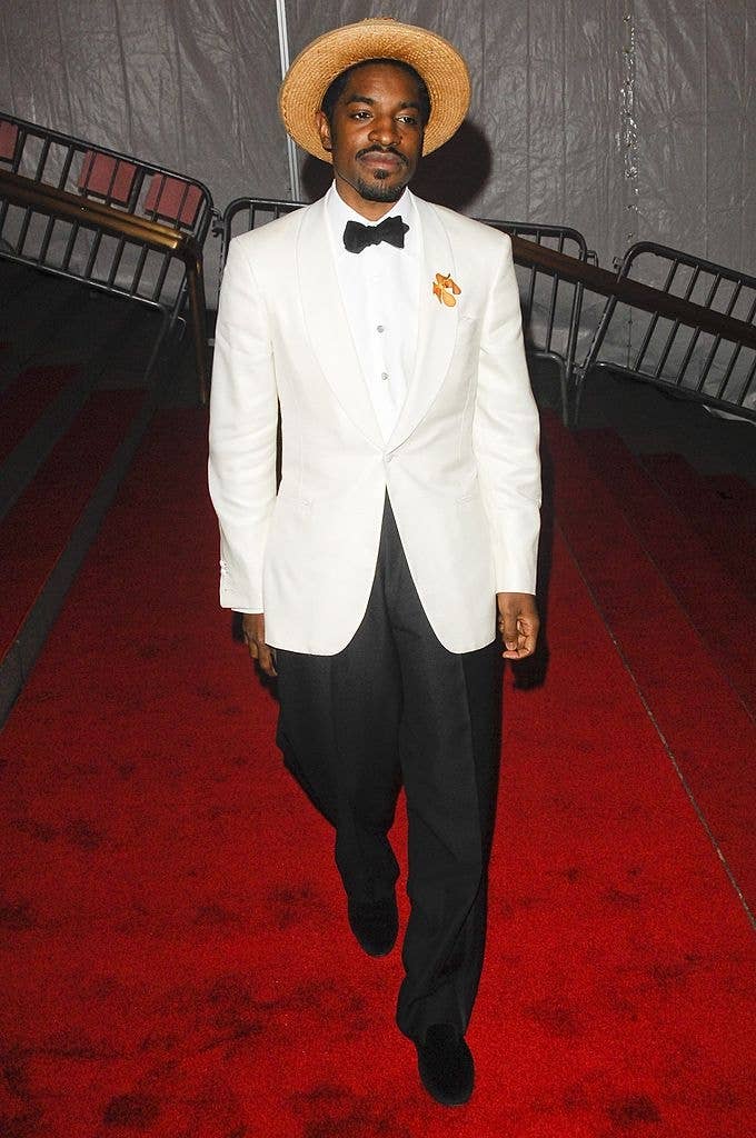 Celebrity in a white tuxedo jacket, black bow tie, and straw hat on the red carpet, walking confidently
