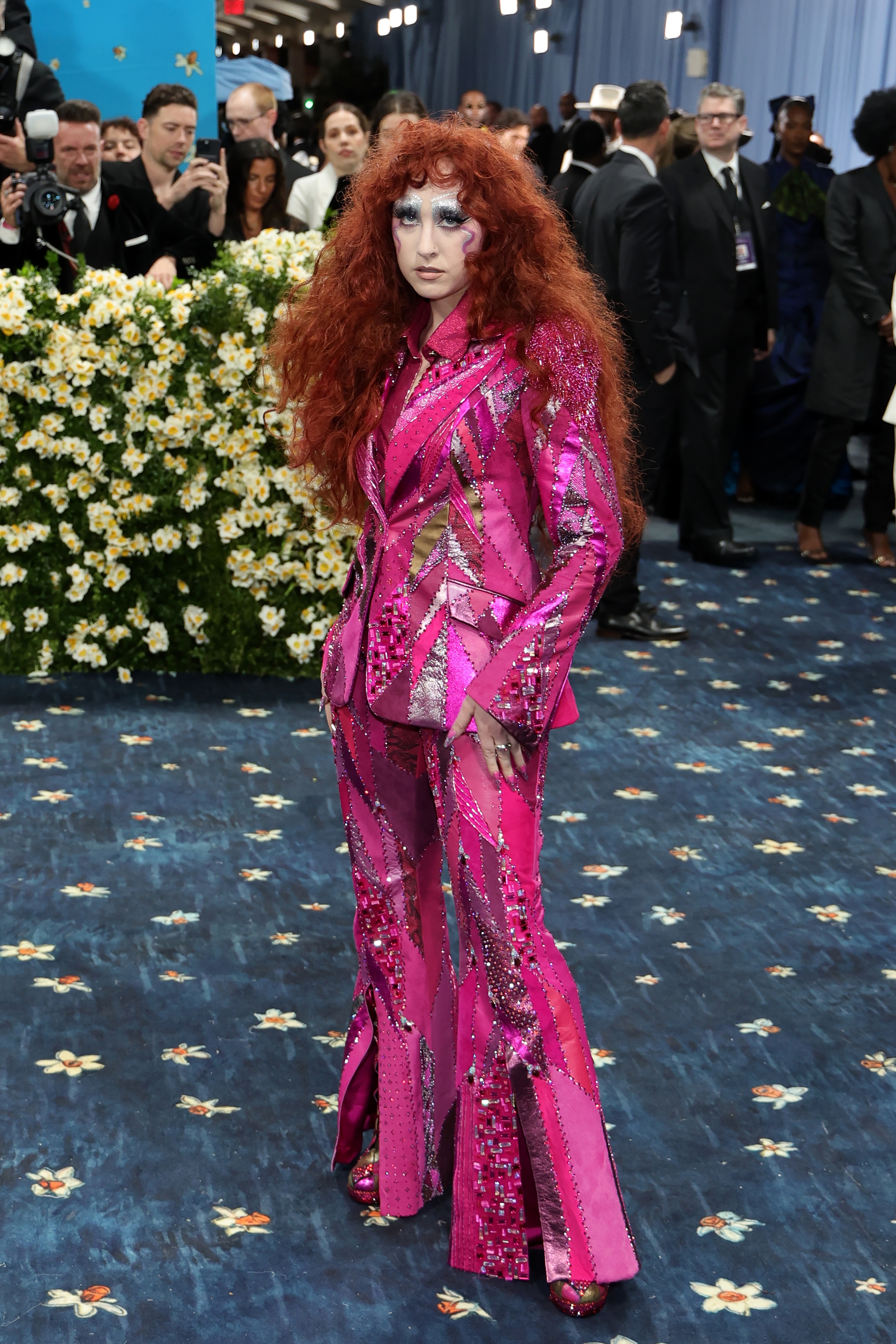 Person with long curly hair in an eye-catching, glam rock-inspired pink sequined suit on the red carpet event