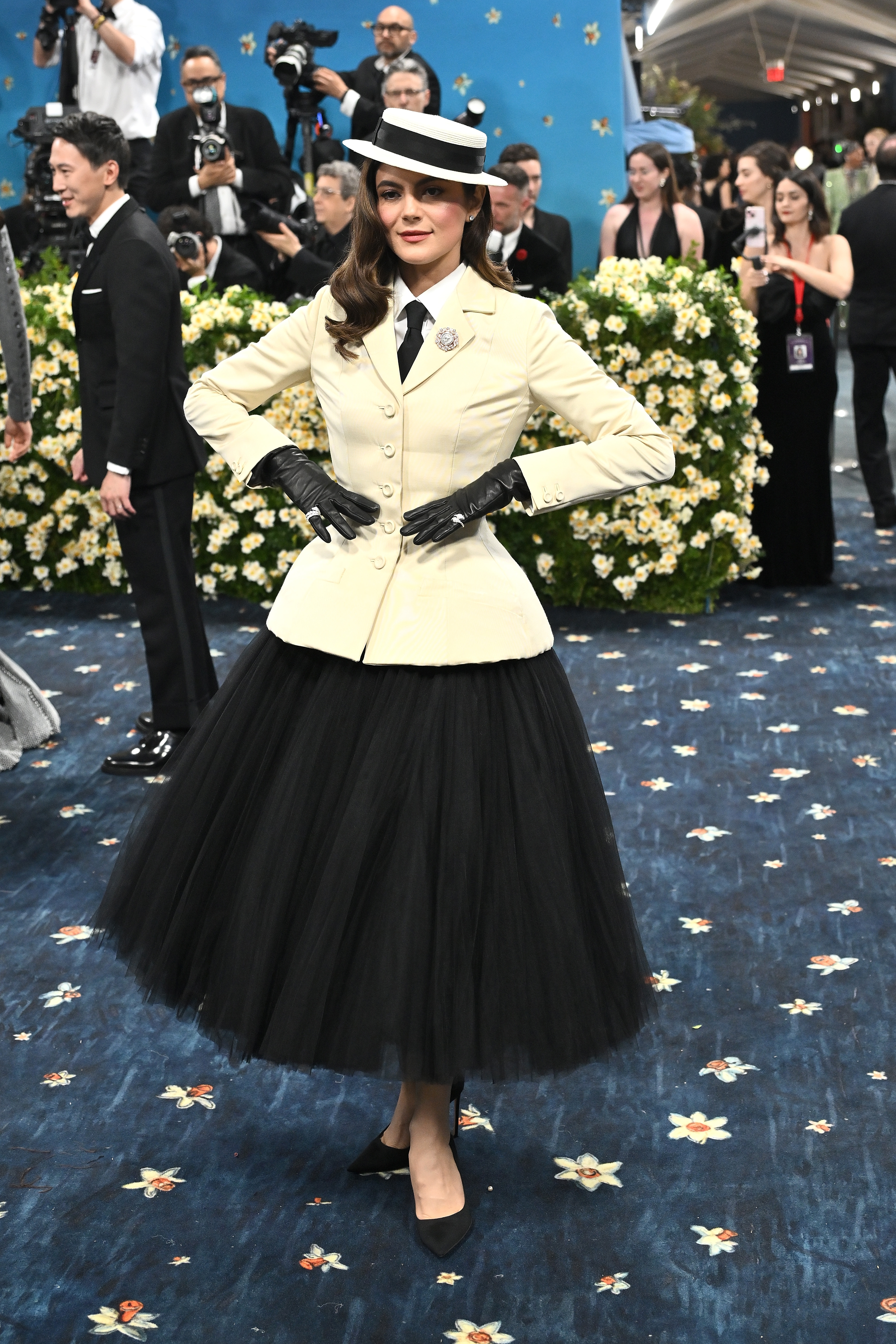 Person in a vintage-inspired outfit with a tailored jacket, black tulle skirt, matching gloves and hat at a formal event