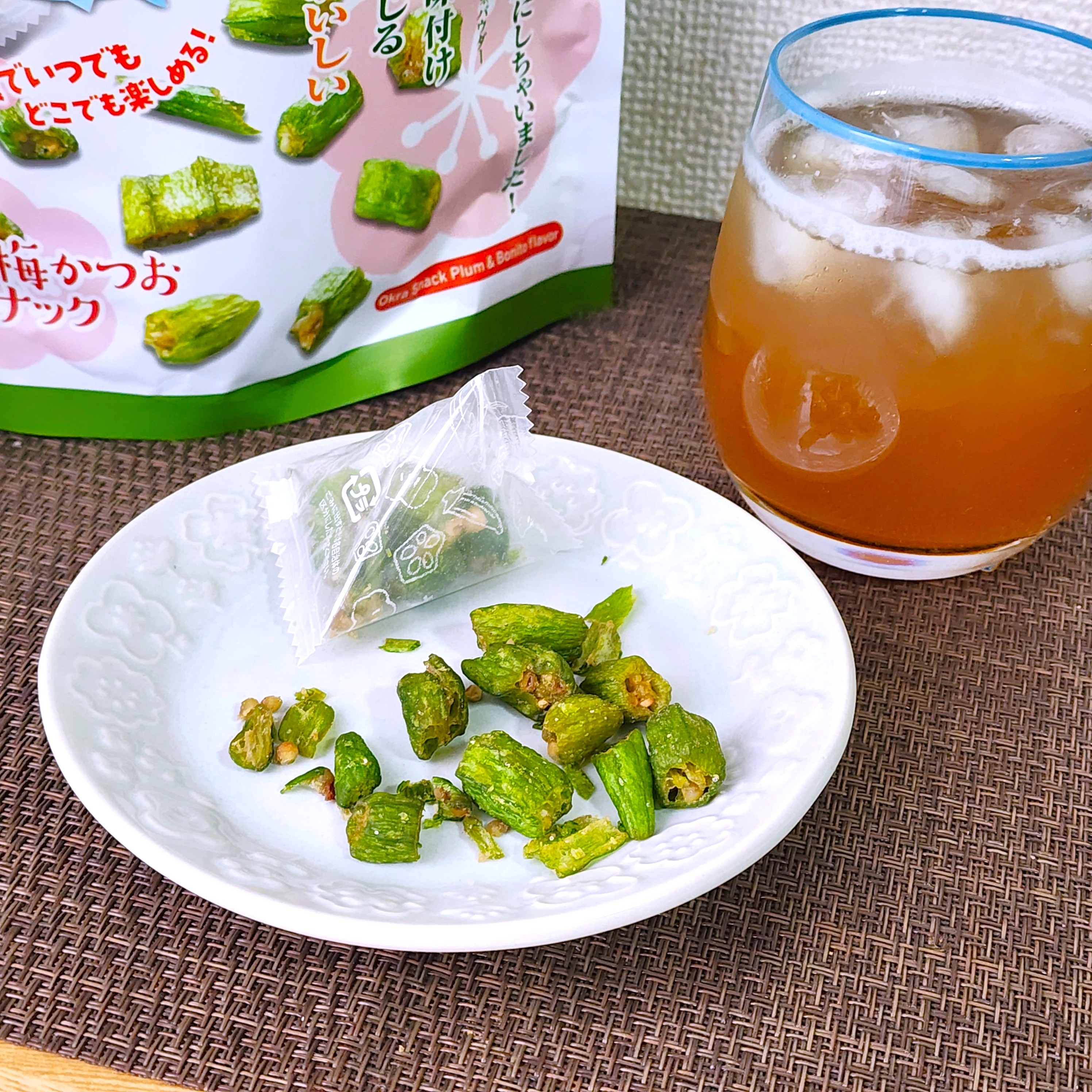 皿におつまみのピーマンとドリンクが置かれ、後ろには袋入りスナックが見える。清涼感のあるテーブル設定。