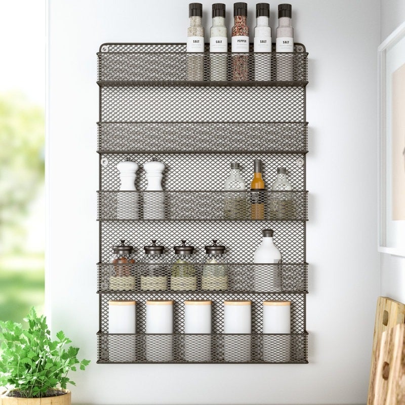 Wall-mounted spice rack with mesh shelves, holding various spice jars and containers