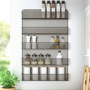 Wall-mounted spice rack with mesh shelves, holding various spice jars and containers