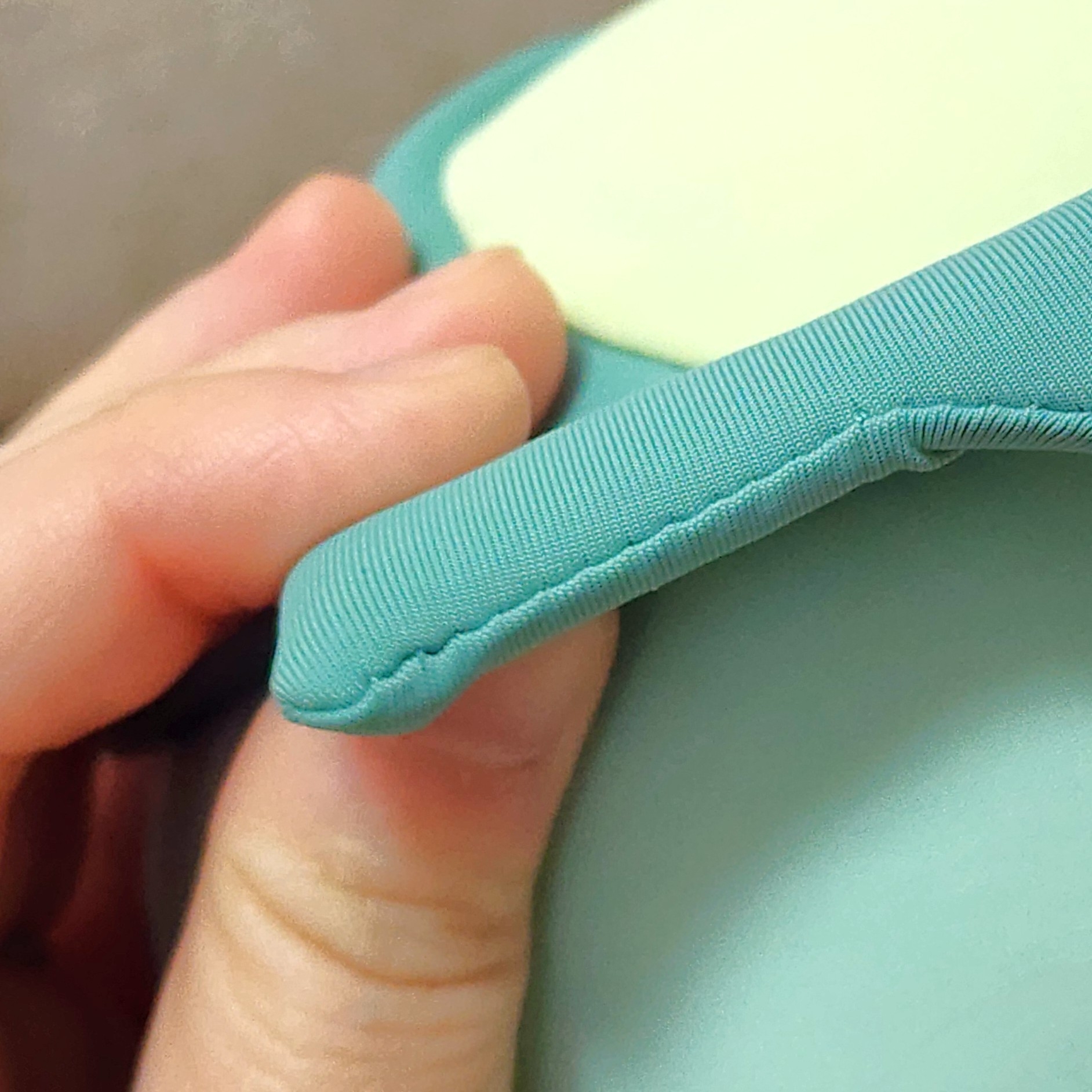 手で持たれている布製のクッションの縁のクローズアップ。柔らかそうな素材が見える。