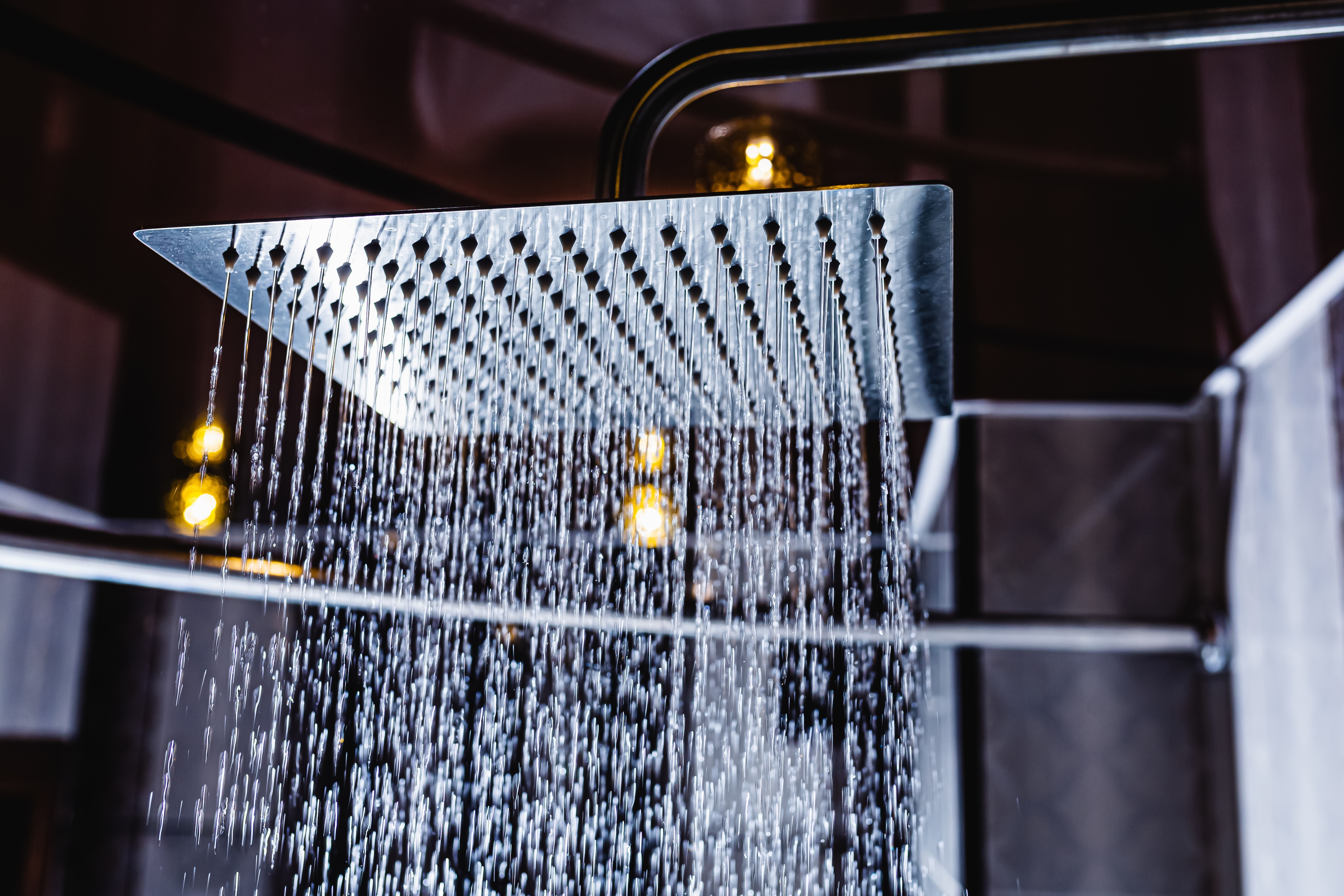 Close-up of a modern square showerhead with water cascading down, set against a blurred bathroom background.