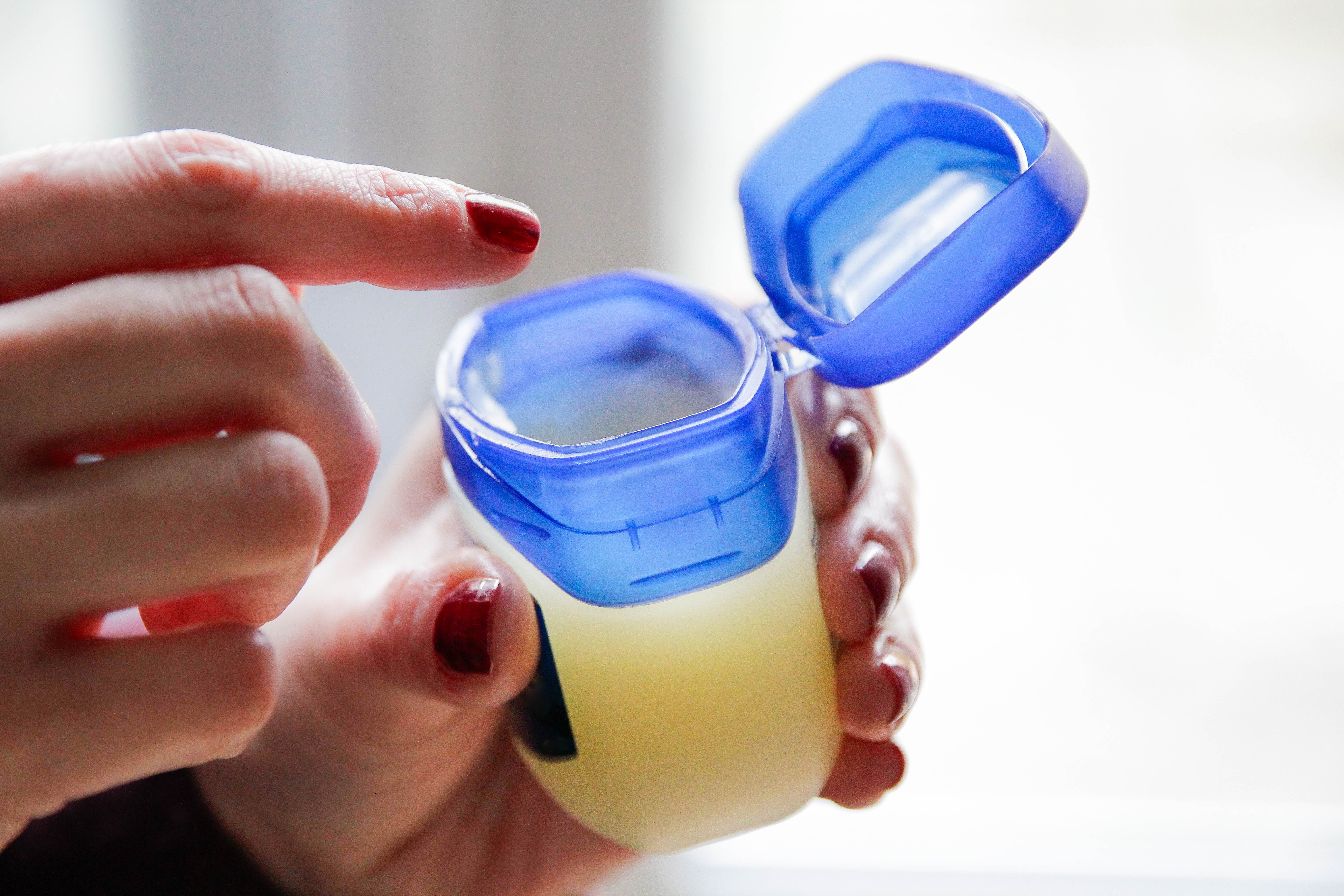 A person holding an open jar of Vaseline.