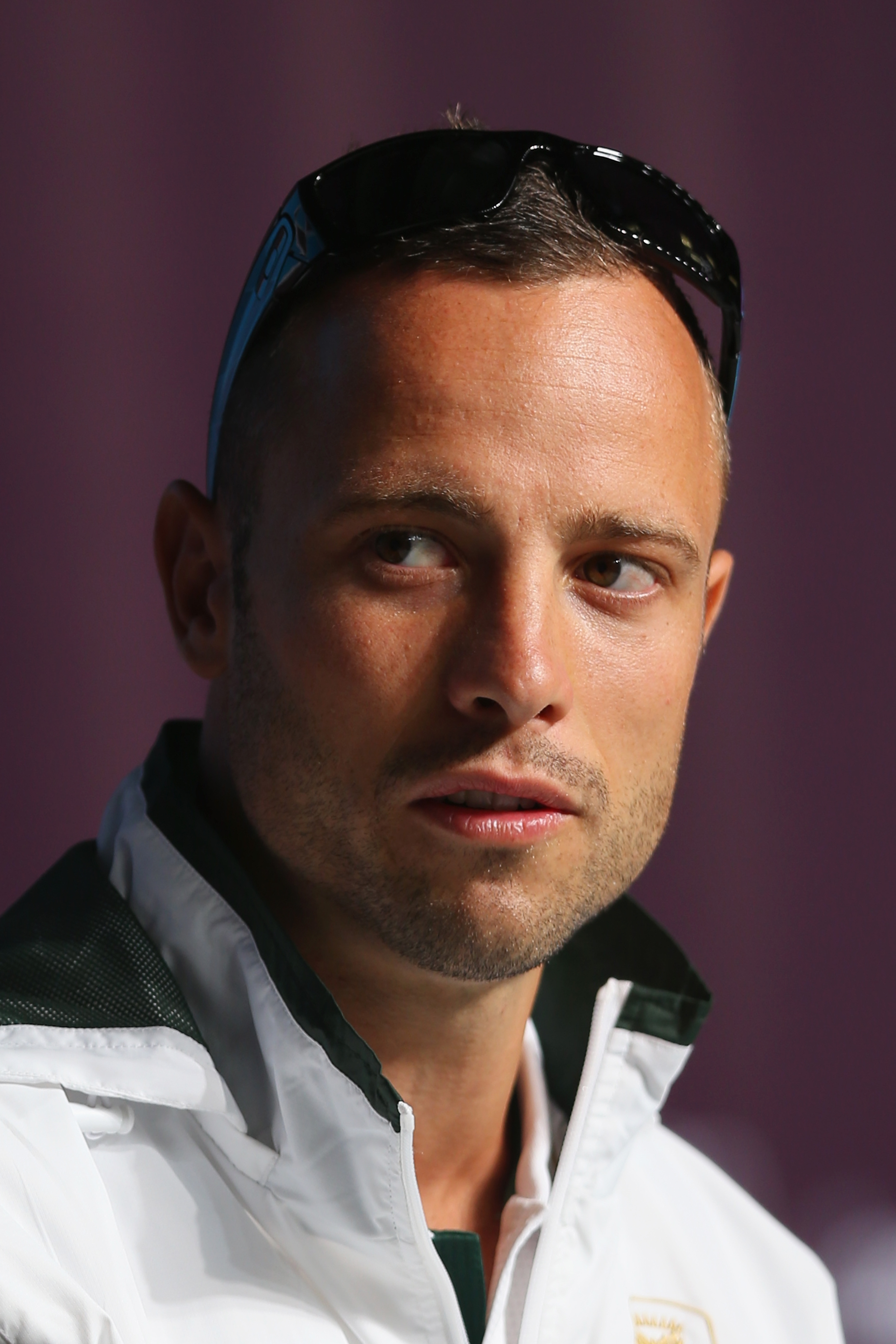 A person in a white athletic jacket with sunglasses on their head, looking off-camera