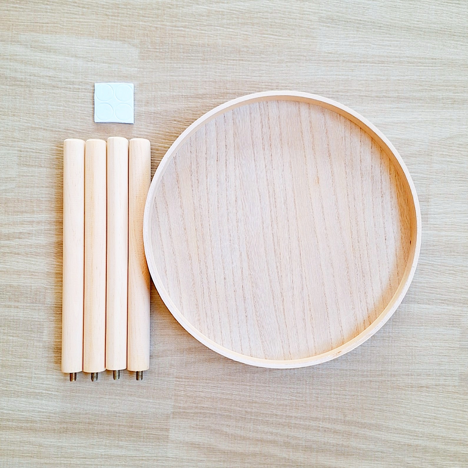 組み立てる前の丸い木製テーブルトップと4本の脚、1つの小さなアクセサリーパーツが並べられている。