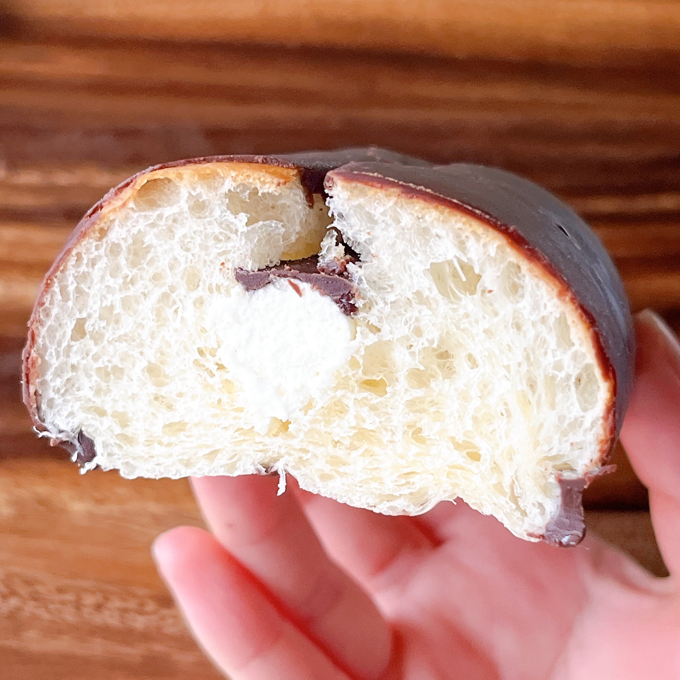手で半分に割られたチョコレートでコーティングされたパン。中にクリームが見える。