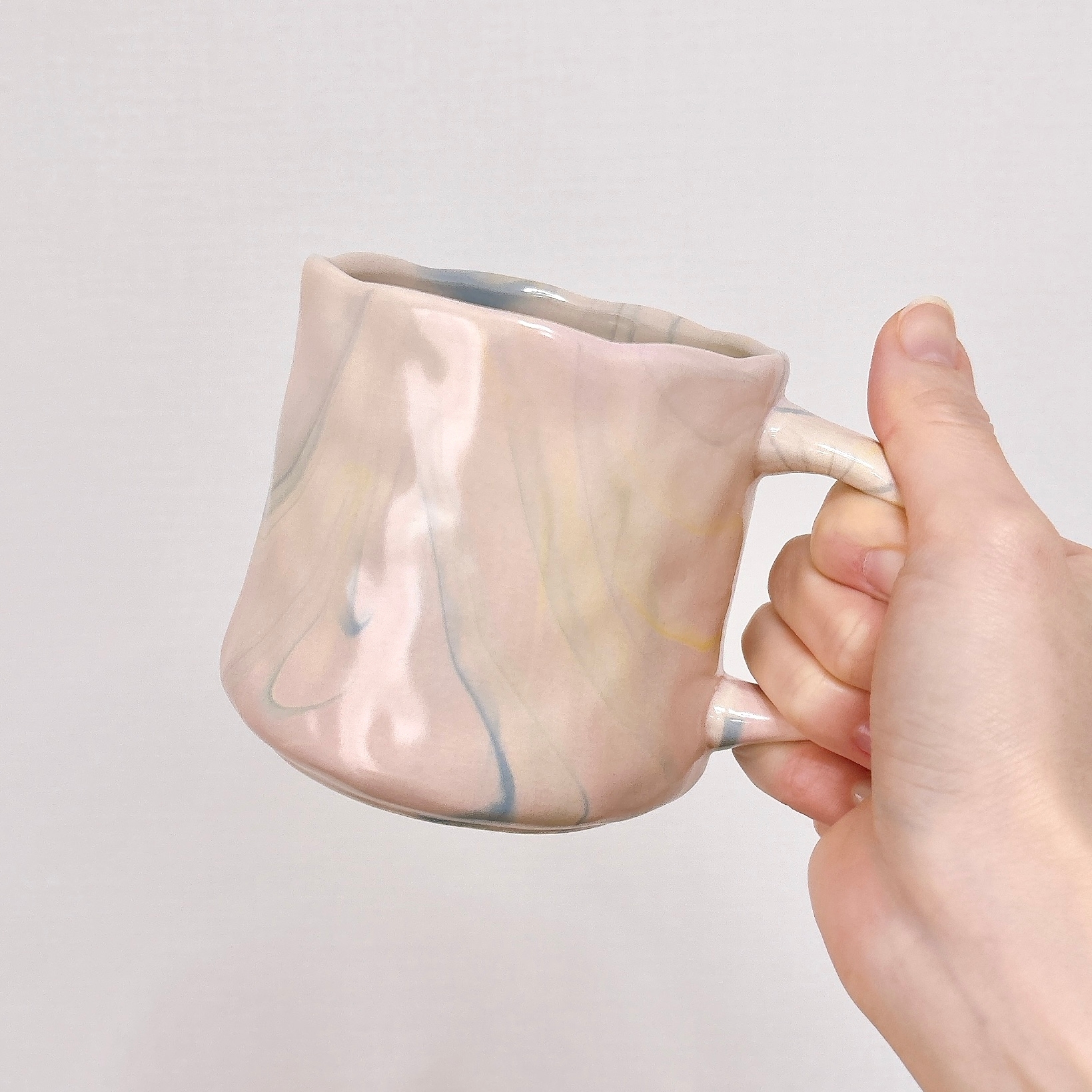 手に持たれたユニークな形状の陶器のマグカップ。