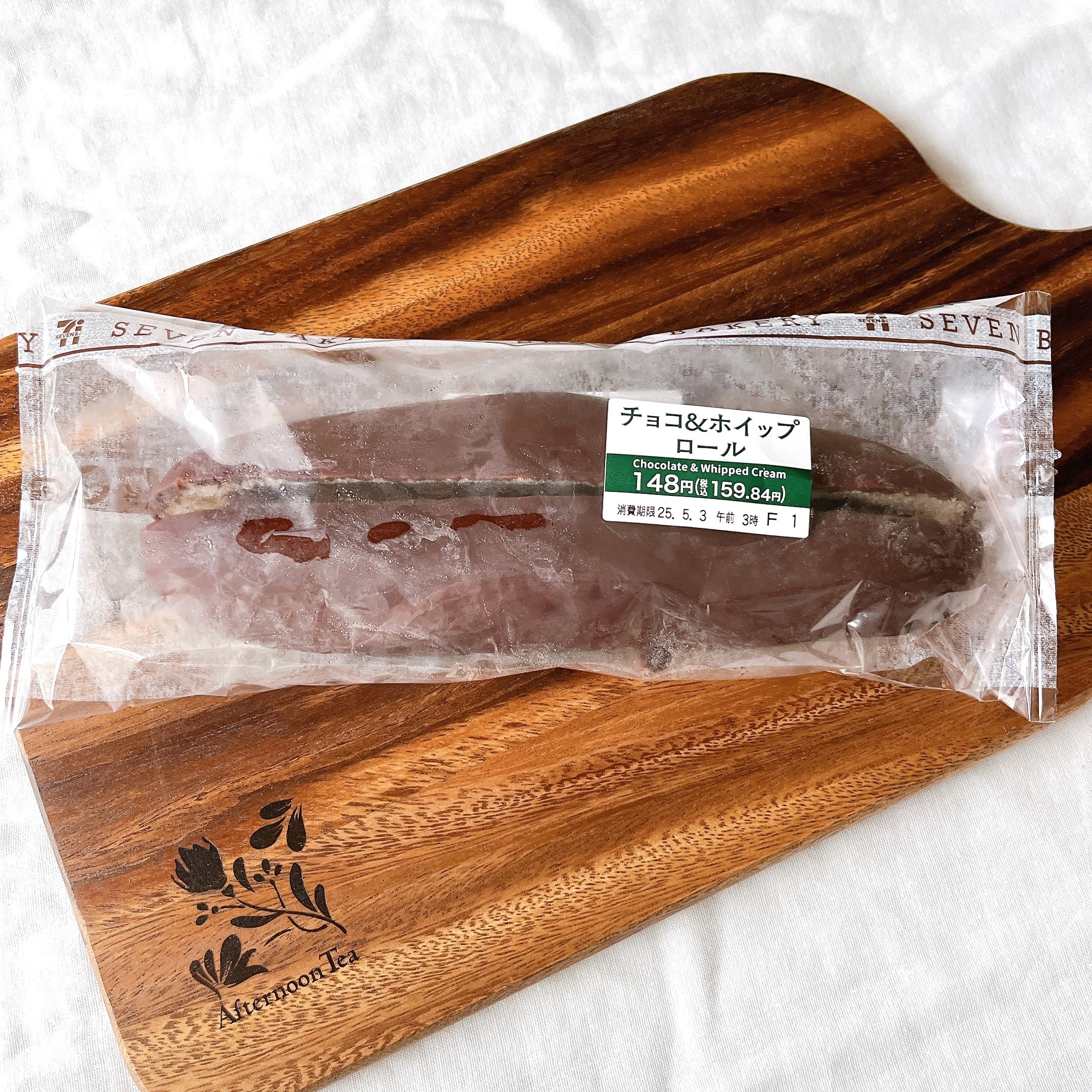 袋に入ったチョコレートホイップクリーム入りロールパンが木製のまな板に置かれている。