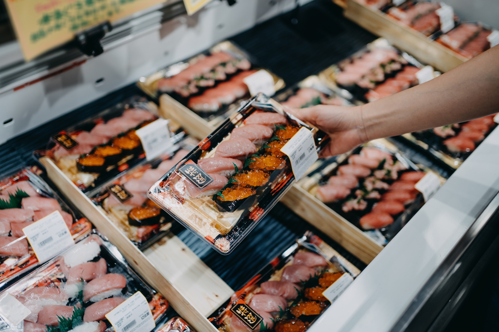 Person picks sushi pack from a display of assorted sushi at a market