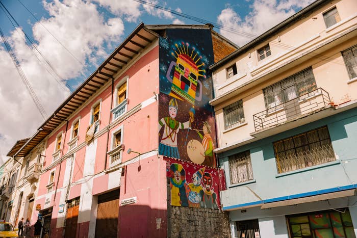 Building with vibrant mural featuring traditional figures and cultural symbols on its side under a partly cloudy sky