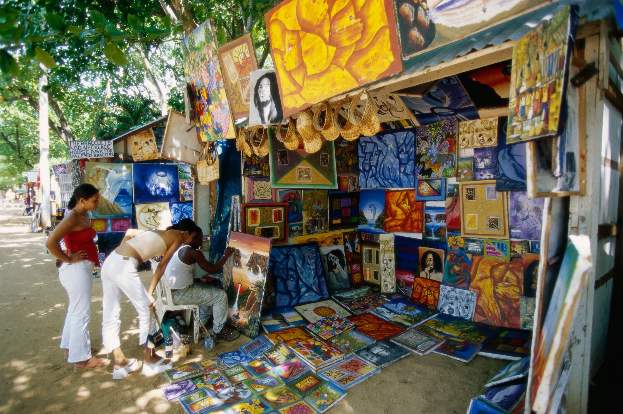 People browsing colorful, diverse paintings at an outdoor art stall