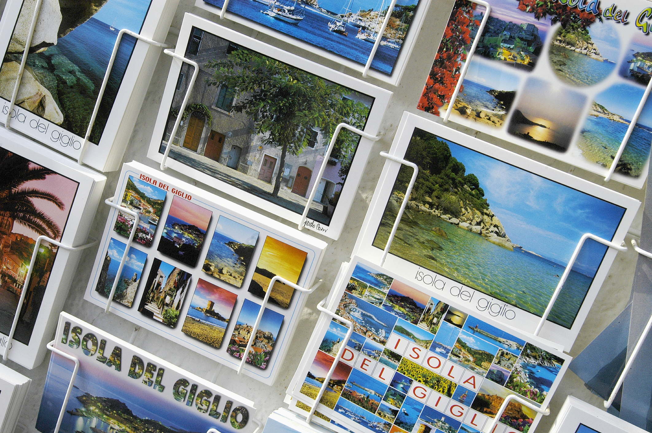 Postcards from Isola del Giglio displayed in a stand, featuring scenic views and attractions of the island