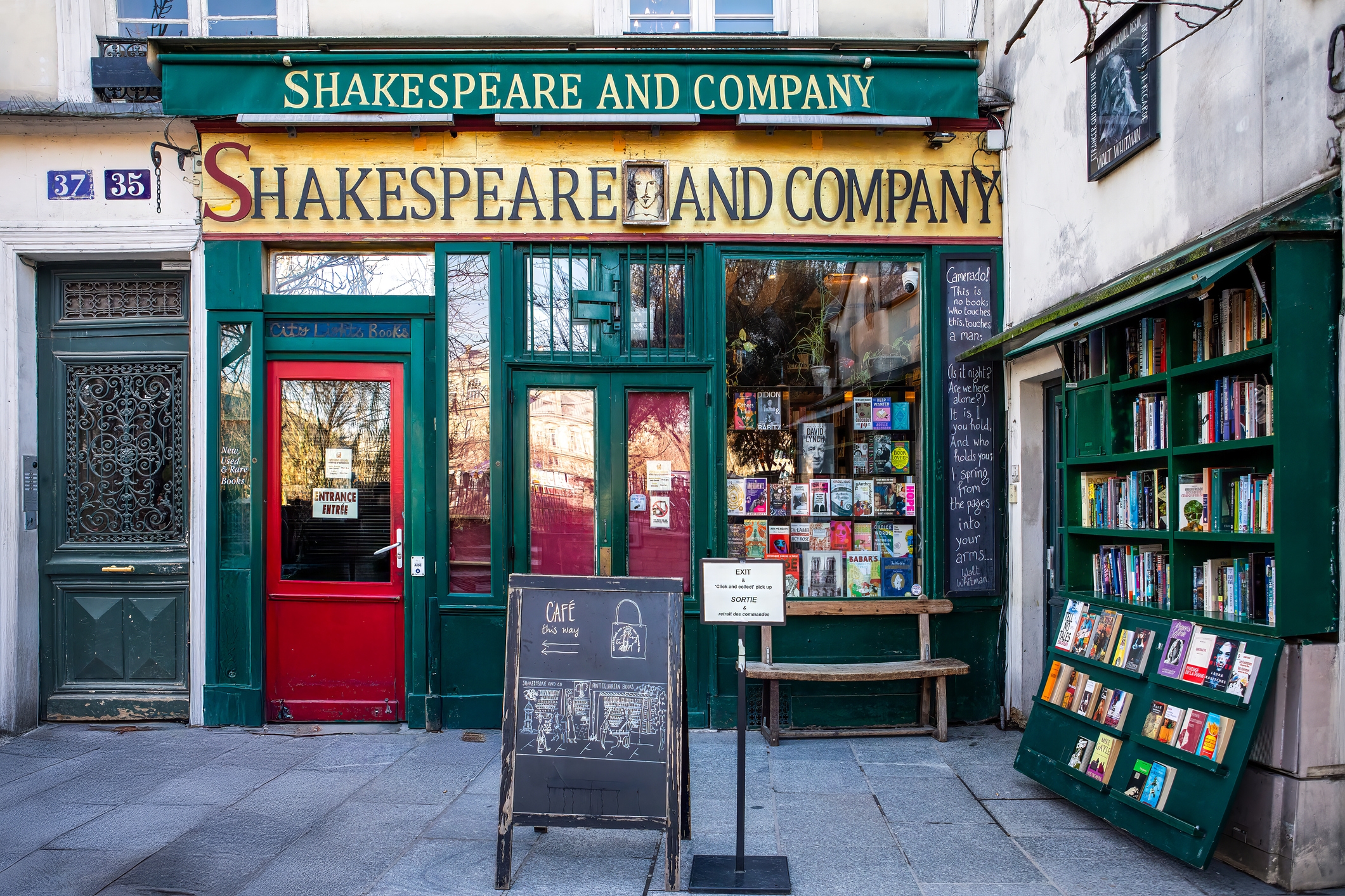 Front view of the Shakespeare and Company bookstore, with books displayed and a signboard outside