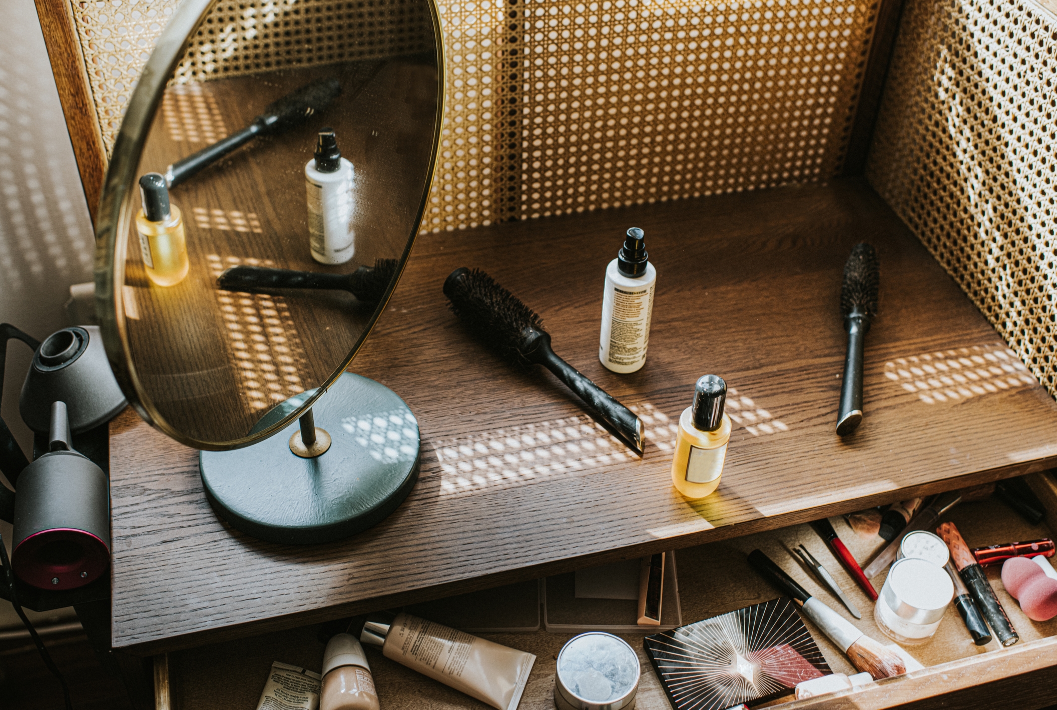Vanity table with a round mirror, various cosmetics, lotions, and brushes scattered on the surface, reflecting a casual morning routine