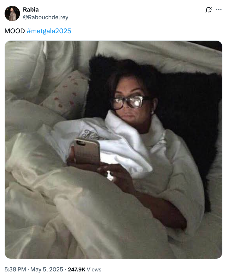 Person in a robe and glasses lying in bed, using a smartphone