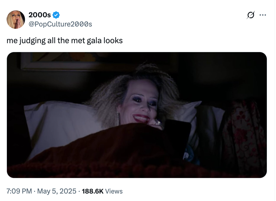 Person with dramatic makeup in bed, smiling at phone. Tweet humorously comments on Met Gala outfits