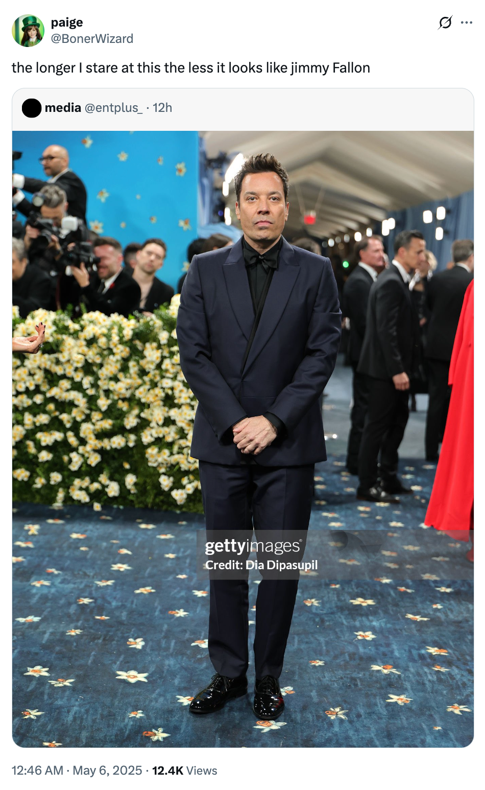 A man in a formal dark suit stands on a floral-patterned carpet at a high-profile event