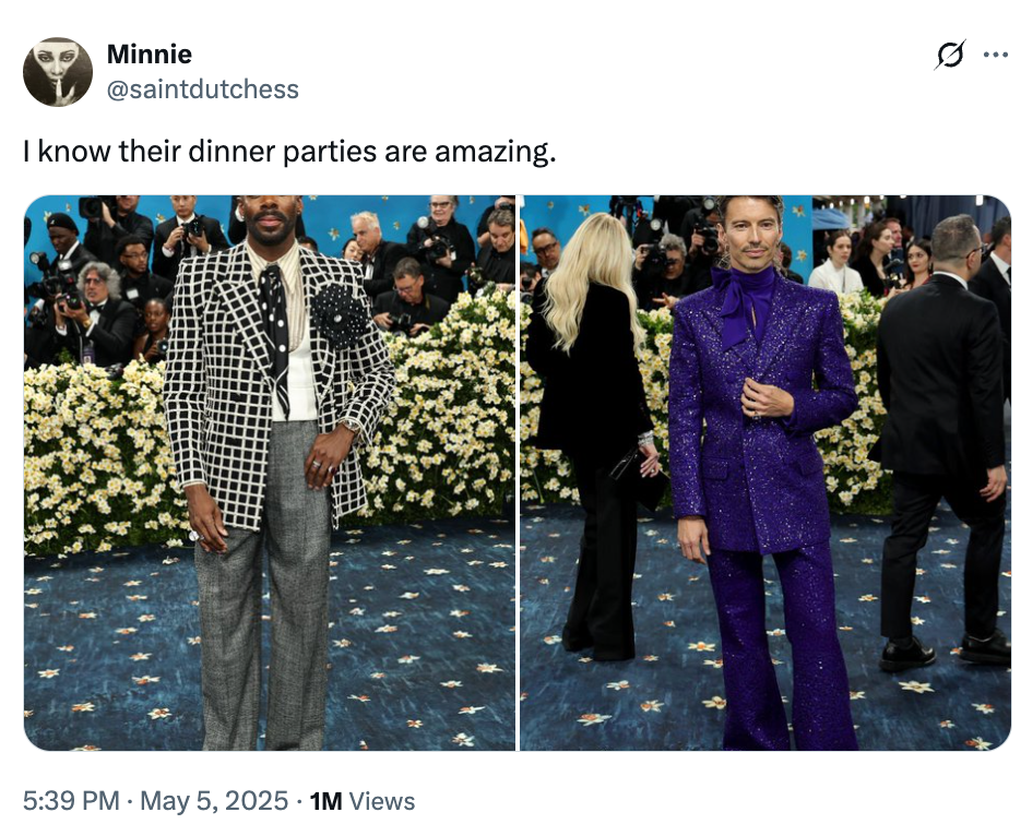 Two people at a formal event; one wears a patterned jacket and trousers, the other a sparkling purple suit. Crowd and floral backdrop present