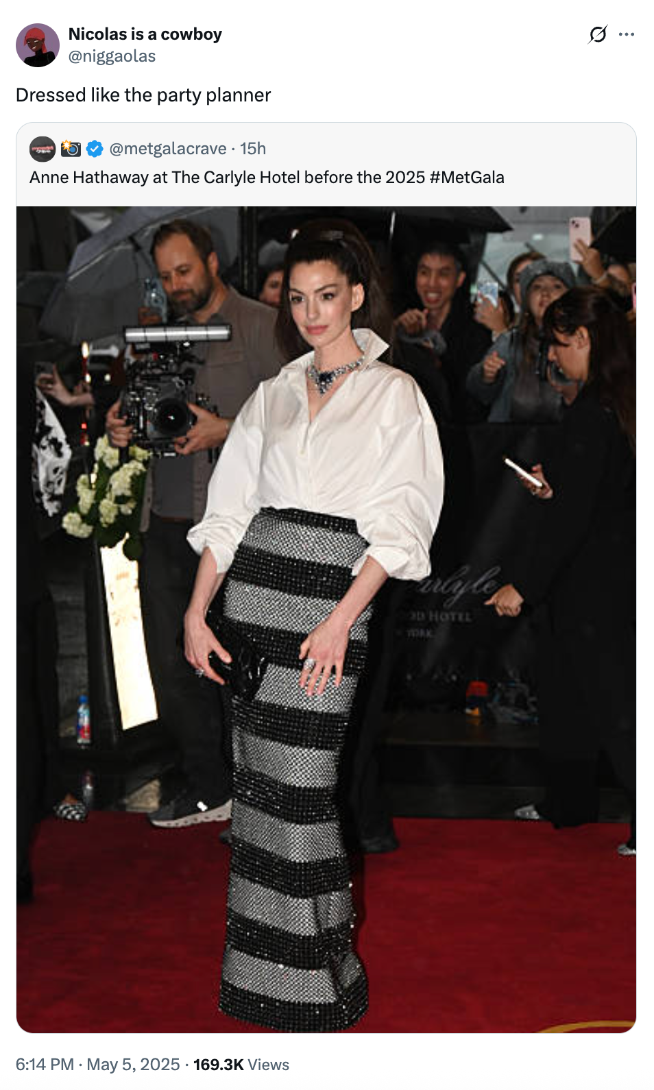 Person on red carpet in an elegant skirt and white blouse poses for photos at a formal event surrounded by media