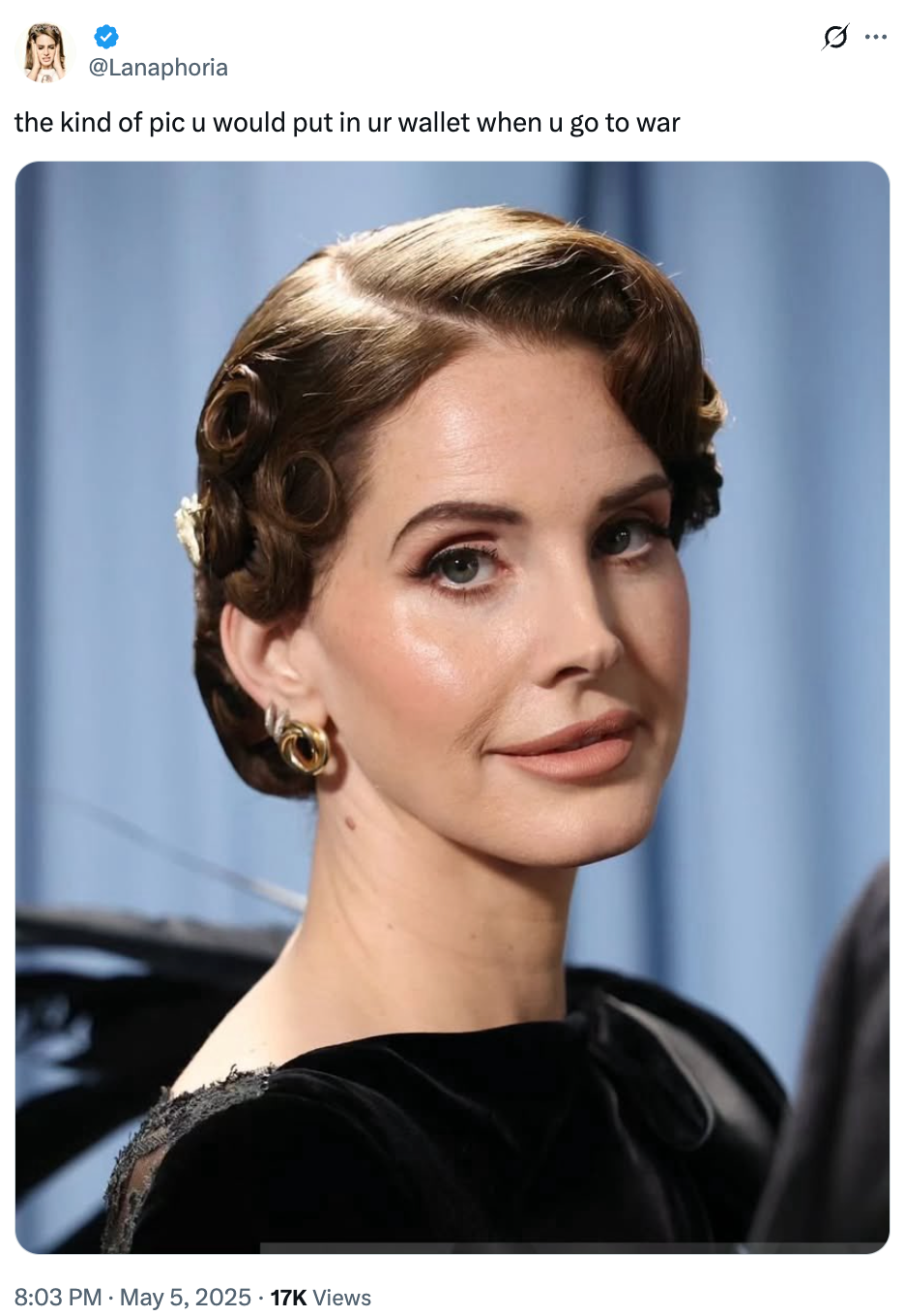 Person with vintage hairstyle and elegant earrings, wearing a classic black dress, poses gracefully