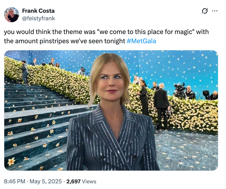 A person on a floral-themed red carpet in a V-neck pinstripe outfit at a gala event, with others and photographers in the background