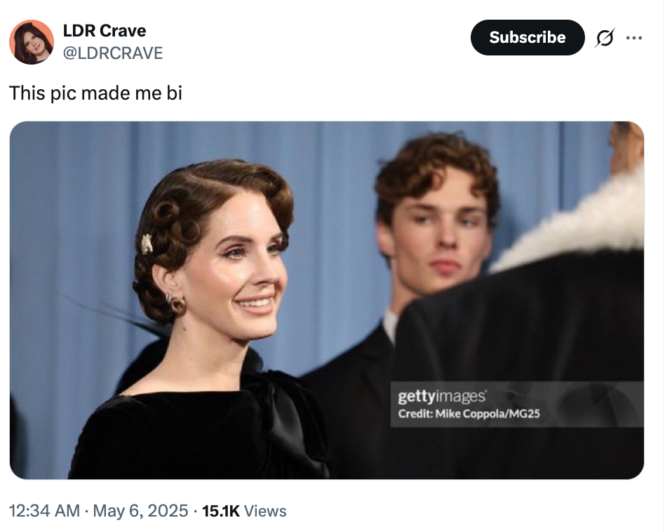Celebrity in elegant black gown smiling at an event, standing near others