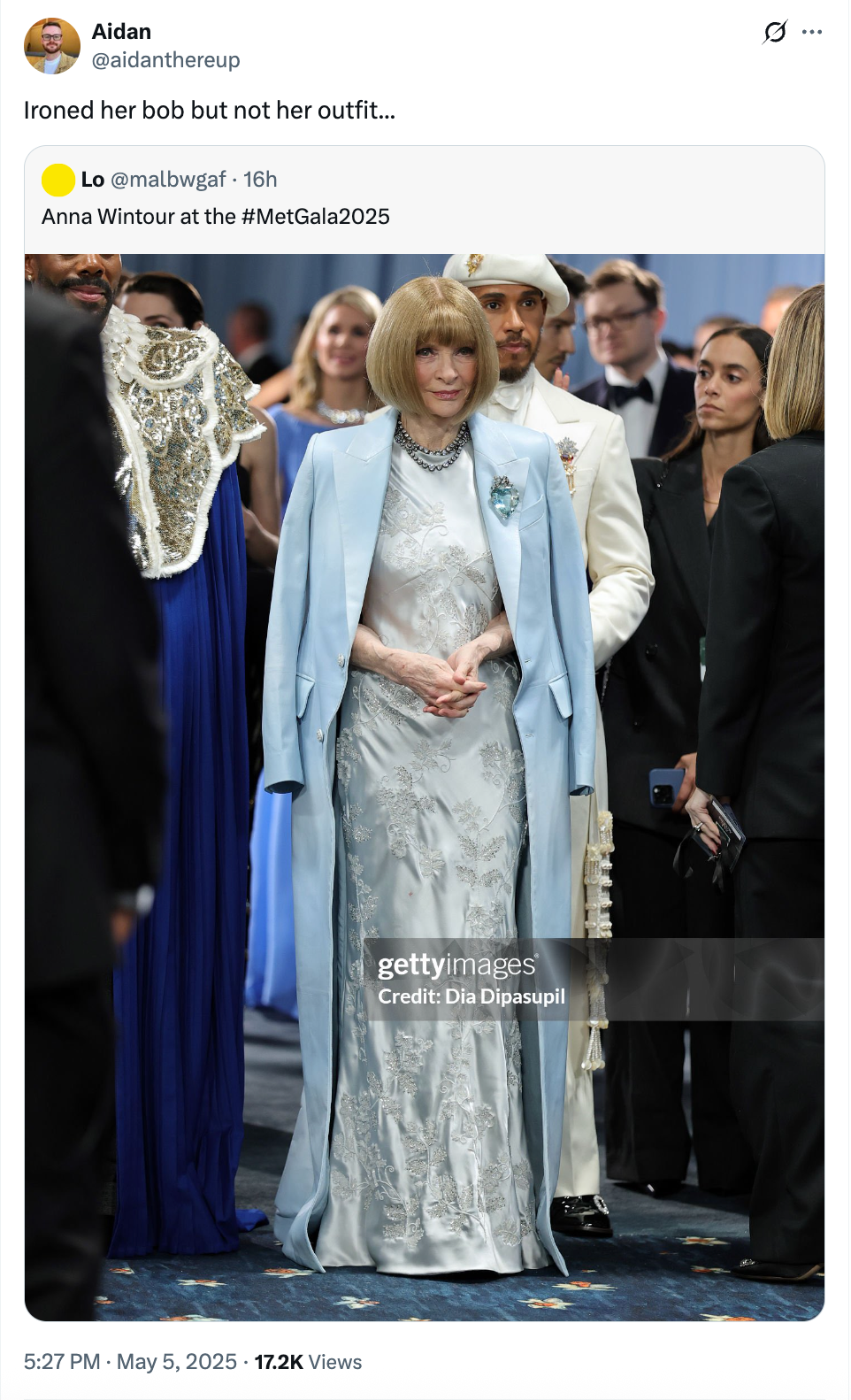 Person in an elegant silver gown with a blue cape, surrounded by others at a formal event