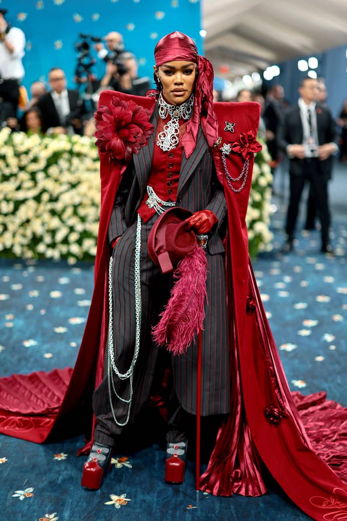 Person wearing an intricate, bold outfit with a long, flowing cape and detailed accessories, posing at a formal event