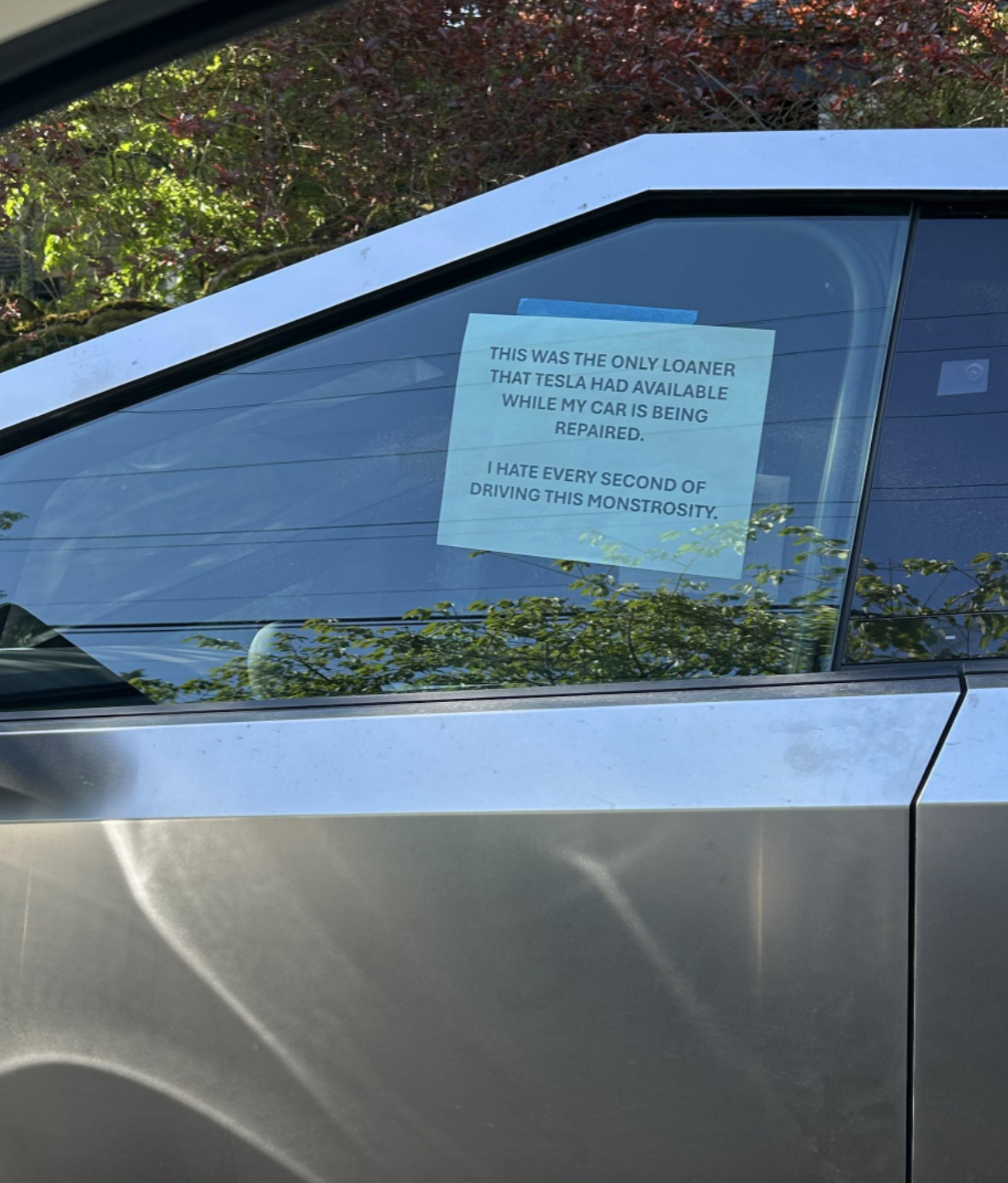 Sign on a cybertruck window reads: "This was the only loaner Tesla had available while my car is being repaired. I hate every second of driving this monstrosity"