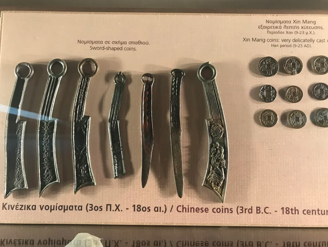Display of ancient Chinese coins, including sword-shaped coins from 3rd century B.C. to 18th century, showcased in a museum