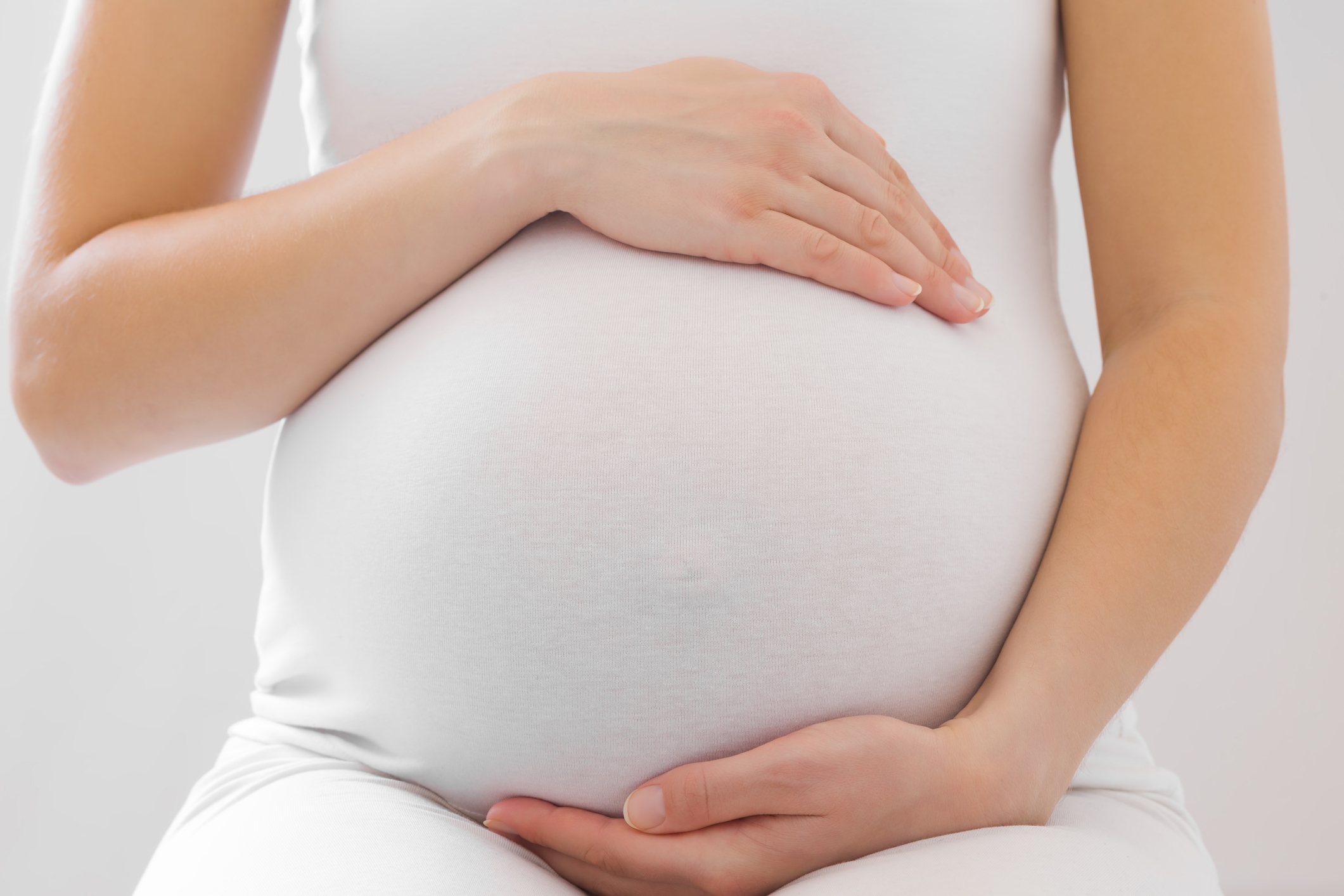 Pregnant person gently cradles their belly with both hands, conveying a sense of care and anticipation