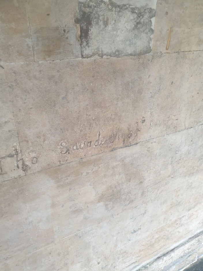 An old wall with faint, carved text that appears to say "Saved 1819." The surface is weathered and textured