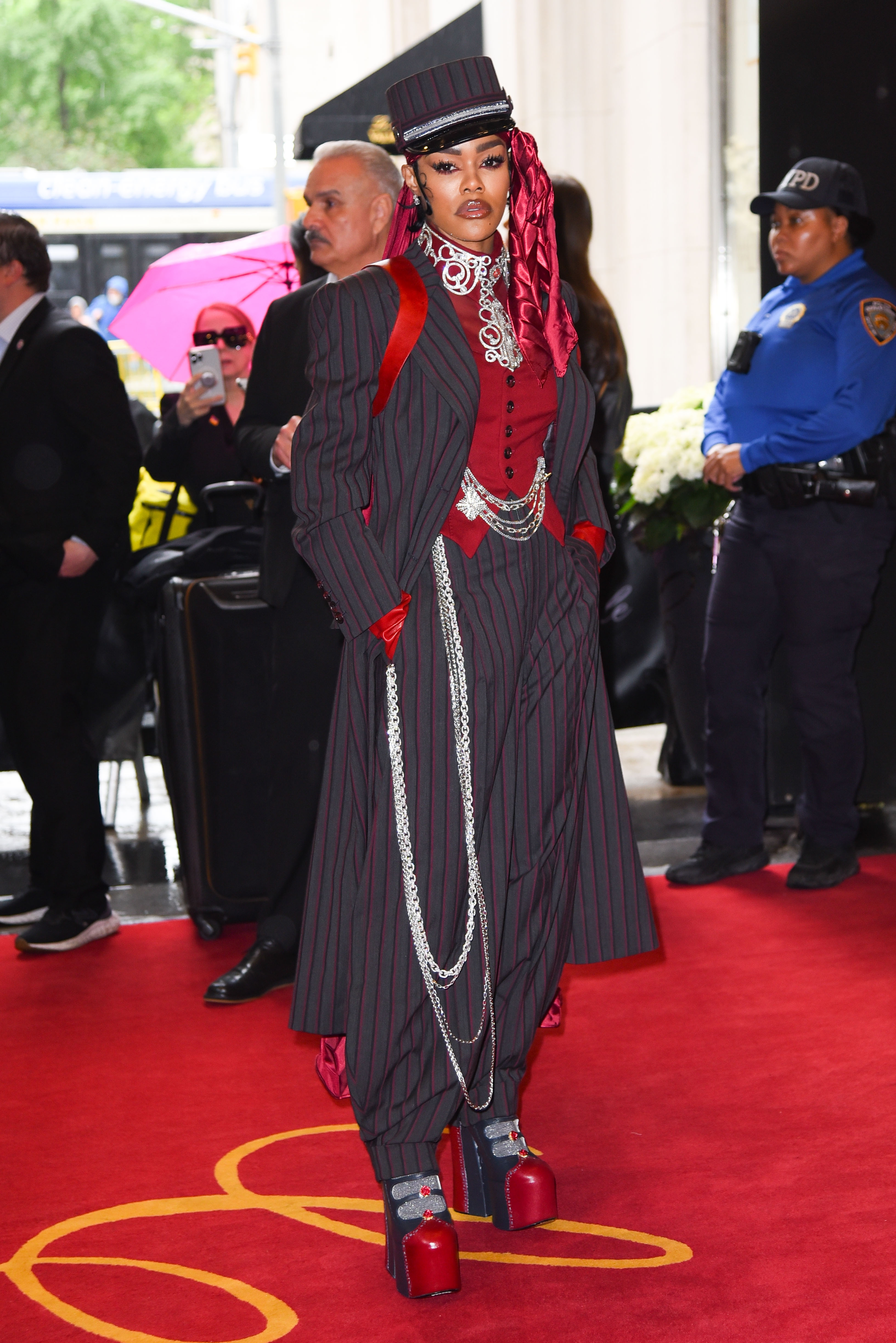 Person in striped suit and top hat with long chains and platform shoes on a red carpet