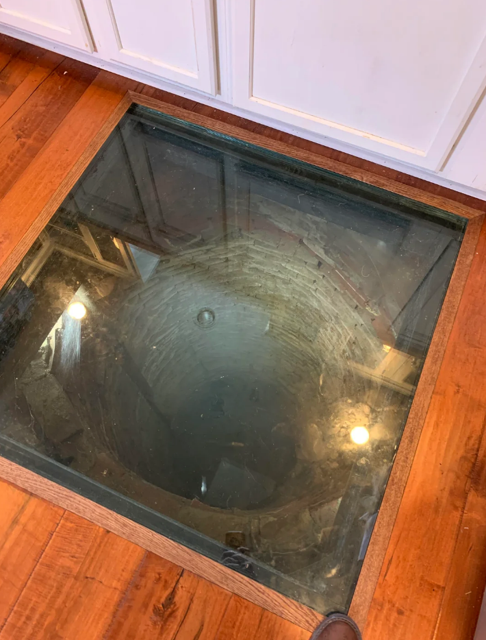 Glass floor panel revealing a view into an old brick well below, set within a wooden floor in a modern interior space