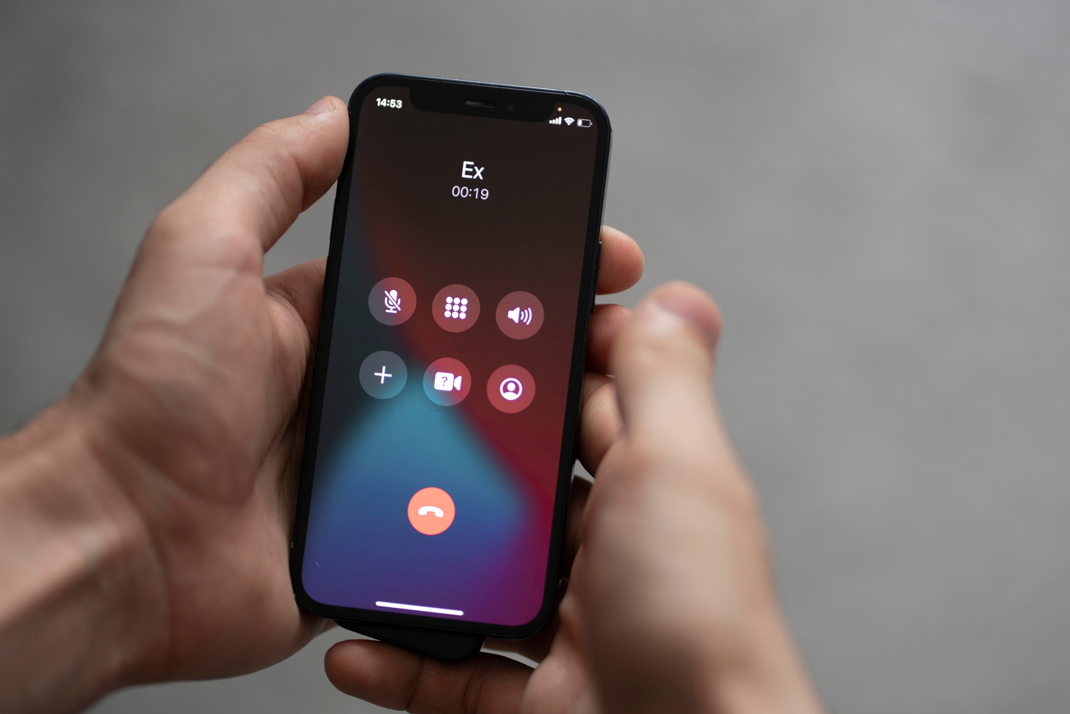 Close-up of a hand holding a phone showing an ongoing call with &quot;Ex.&quot; Various call options are visible on the screen