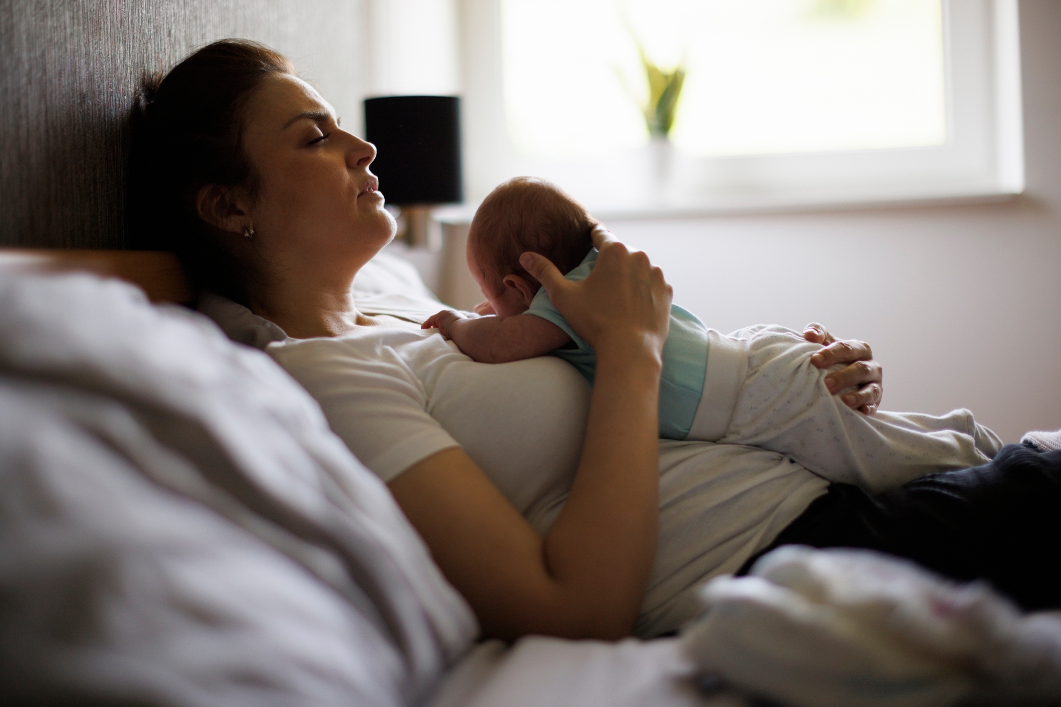A woman is lying in bed, holding a baby resting on her chest, conveying a serene and intimate moment