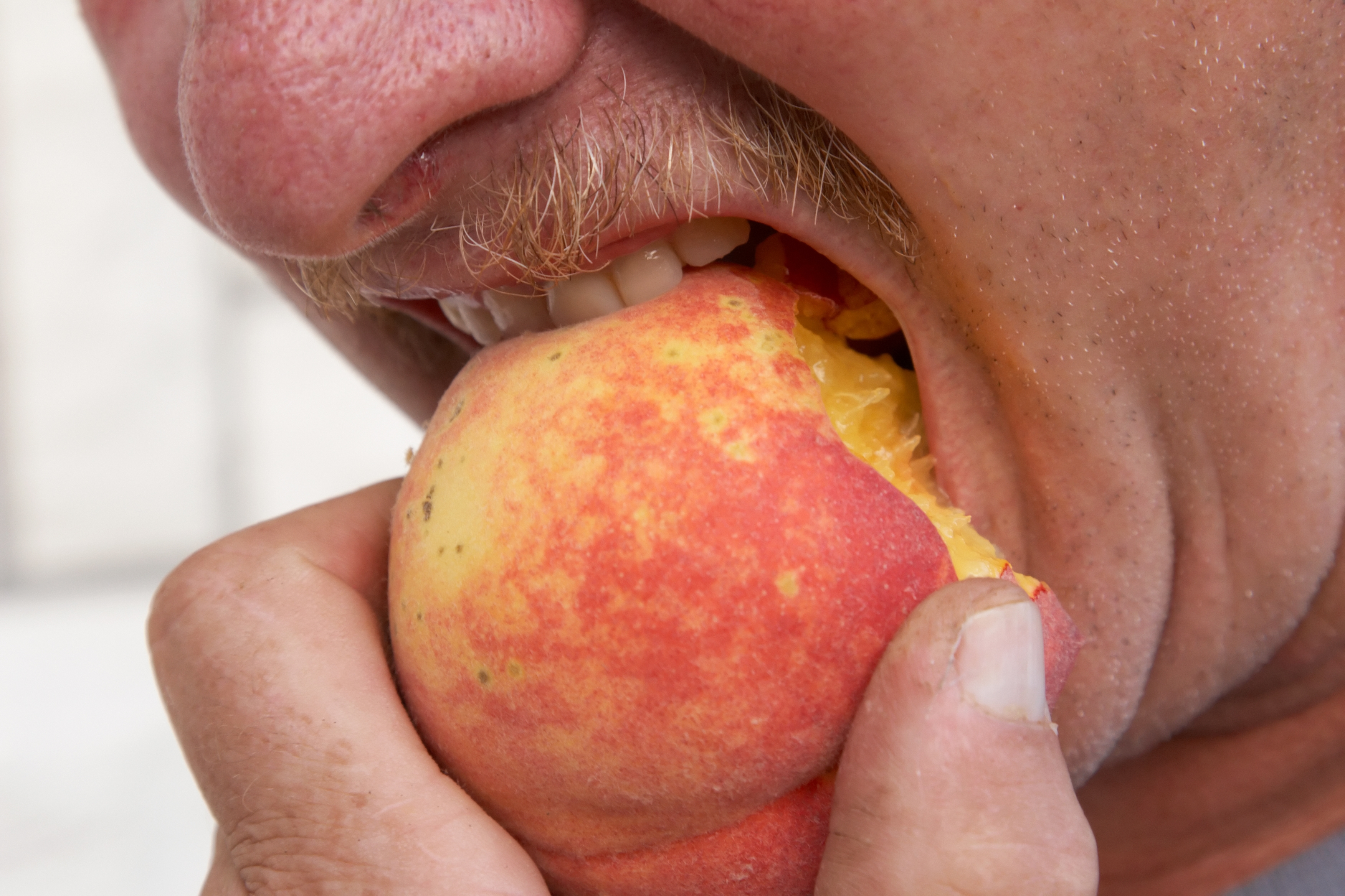Person taking a big bite of a ripe peach, showing enthusiasm and enjoyment