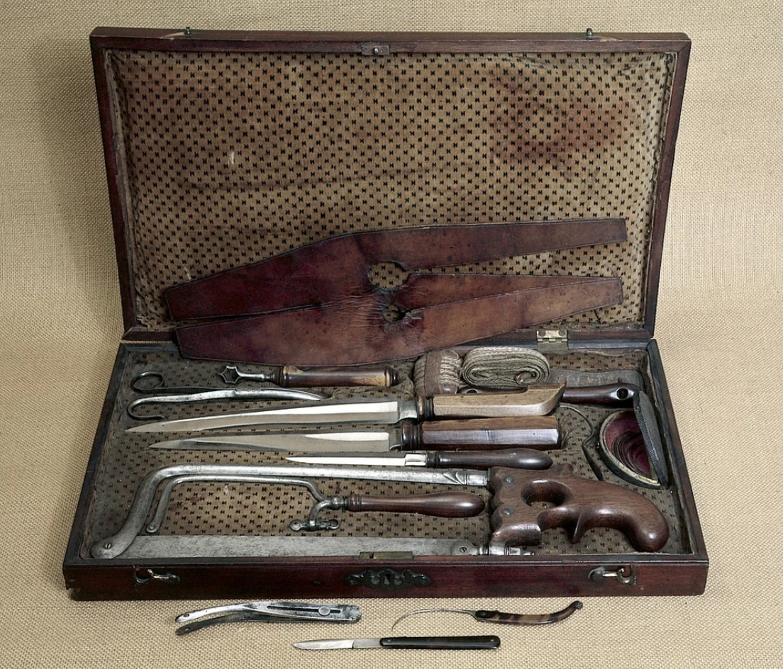 Open vintage surgical set with assorted medical tools, including saws, scalpels, and clamps, displayed in a lined wooden case